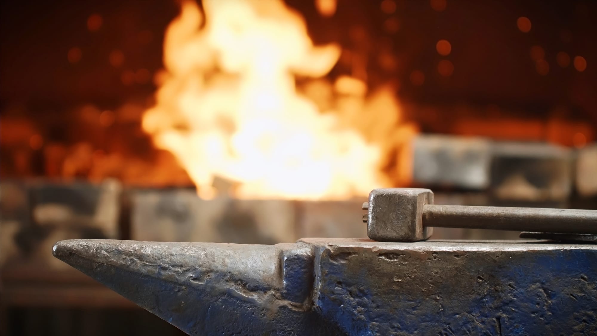 Blacksmith's hammer resting on an anvil in front of a forge fire